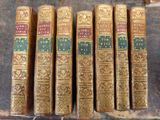 six old books are lined up on a shelf next to a book case