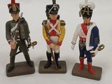 three figurines of soldiers in uniforms and weapons on a white surface