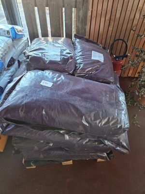 a pile of bags of pillows on a pallet next to a potted plant