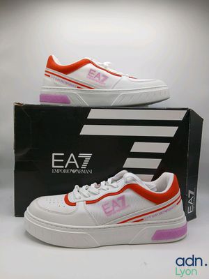 une image représentant une paire de baskets blanches et orange posées sur une boîte