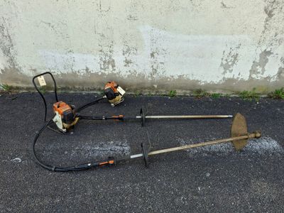 two lawn mowers on the ground next to a wall