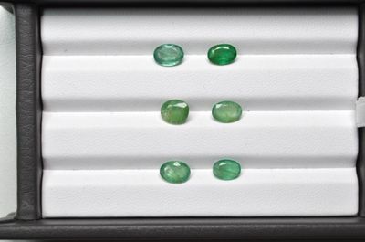 trois émeraudes vertes dans un écrin noir posé sur une surface blanche