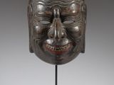 a bronze mask on a black stand with a white background