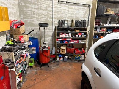 une voiture blanche garée dans un garage, à côté d'une étagère remplie d'outils