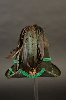 un chapeau vert orné de plumes, posé sur un socle en verre