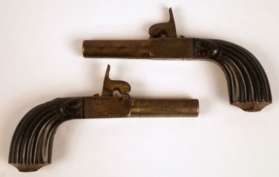 une paire de pistolets anciens en laiton sur fond blanc, avec un chat posé sur l'un d'eux
