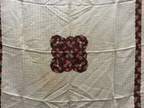 an image of a white quilt with a red and green flower on it