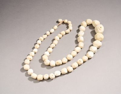 une image représentant un collier de perles blanches posé sur une surface grise