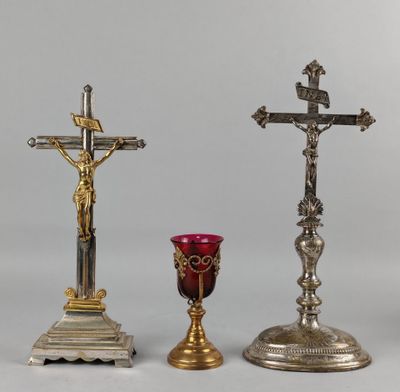 deux croix en argent et en or et un verre rouge posés sur une table