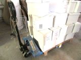 une pile de cartons posée sur une palette, à côté d'un diable