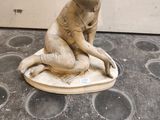 une statue représentant un garçon assis sur une assiette posée par terre