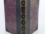 un vieux livre à la couverture violette posé sur une table blanche