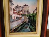 an oil painting of a street scene in a wooden frame on a shelf