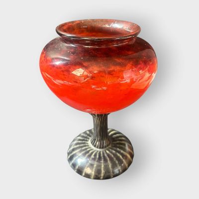 un vase rouge posé sur un socle en métal