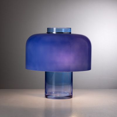 une lampe de table en verre bleu posée sur une table blanche