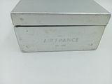 une boîte métallique argentée portant l'inscription « Air France », posée sur une surface blanche