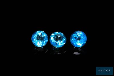 three blue topaz gems in a row against a black background