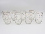 six verres parsemés de points dorés sont alignés sur une surface blanche