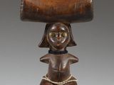 an old wooden figurine of a woman holding a large piece of wood on her head