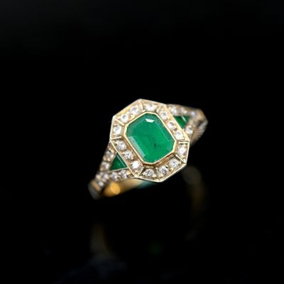an emerald and diamond ring on a black surface
