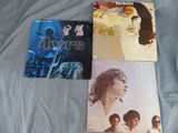 trois albums des Doors sont posés sur un lit recouvert d'un drap bleu