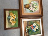 trois tableaux accrochés au mur au-dessus d'un vase de fleurs