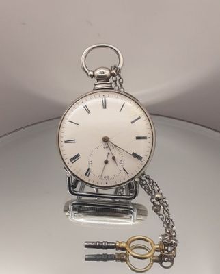 une montre de poche en argent avec une clé, posée sur une table