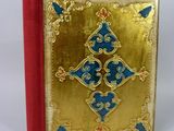un livre doré à la couverture bleue et rouge posé sur une surface blanche