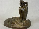 bronze statue of a woman sitting on a rock with her hands on her head