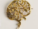 une image d'une broche en or avec une perle au centre