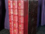 trois livres rouges posés sur une table noire, à côté d'un rideau violet