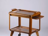 un ancien chariot de service en bois muni de deux plateaux et monté sur roulettes