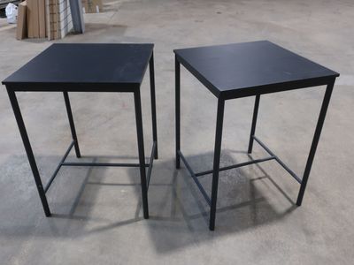 une paire de tables d'appoint en métal noir posées sur un sol en béton dans une zone d'entrepôt