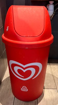 une poubelle rouge sur laquelle est collé un autocollant en forme de cœur