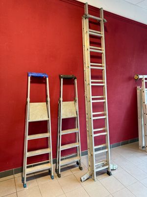 Plusieurs échelles sont appuyées contre un mur rouge dans une pièce.