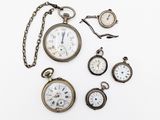 un assortiment de montres de poche anciennes et une chaîne posées sur une surface blanche