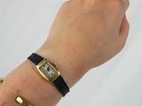 wrist shot of a woman wearing a gold watch and black leather bracelet