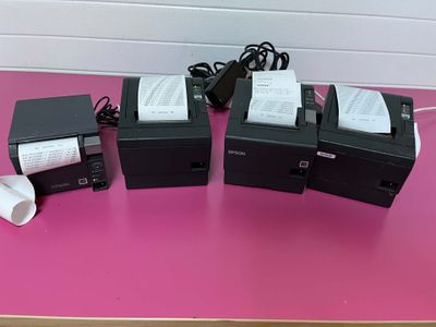 trois imprimantes posées sur une table rose, à côté d'un rouleau de papier