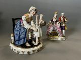 two figurines of women and a cat are sitting on a chair