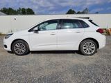 La voiture blanche est garée sur le parking, à côté d'une clôture.