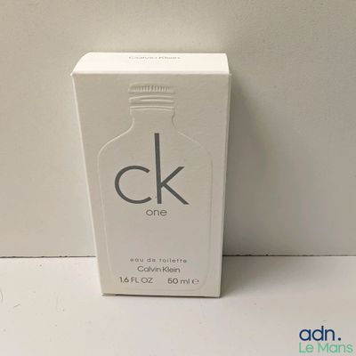 un flacon de parfum dans une boîte blanche, posé sur une surface blanche
