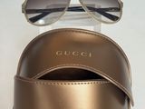 Des lunettes de soleil Gucci et leur étui posés sur une table blanche, sur fond blanc