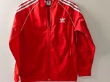 une veste Adidas rouge à rayures blanches suspendue à un cintre