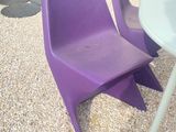 deux chaises violettes et une table à l'extérieur, sur le gravier