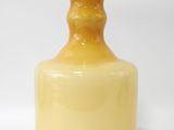 une bouteille en verre jaune posée sur une surface blanche