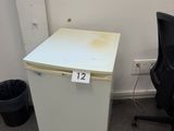 a small white refrigerator next to a black chair in a room