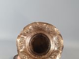 a hand that is holding a silver vase on a table