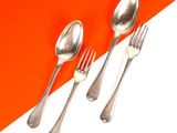 trois cuillères en argent et deux cuillères en argent sur un fond orange et blanc