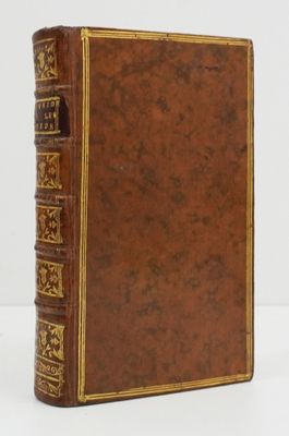 un vieux livre marron aux tranches dorées posé sur une table blanche