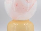 a close up of a yellow vase with a pink marble ball on top